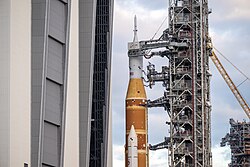 A 322-foot-tall orange and white rocket, the Space Launch System, just outside the doors of the Vehicle Assembly Building, Kennedy Space Center, in January 2026